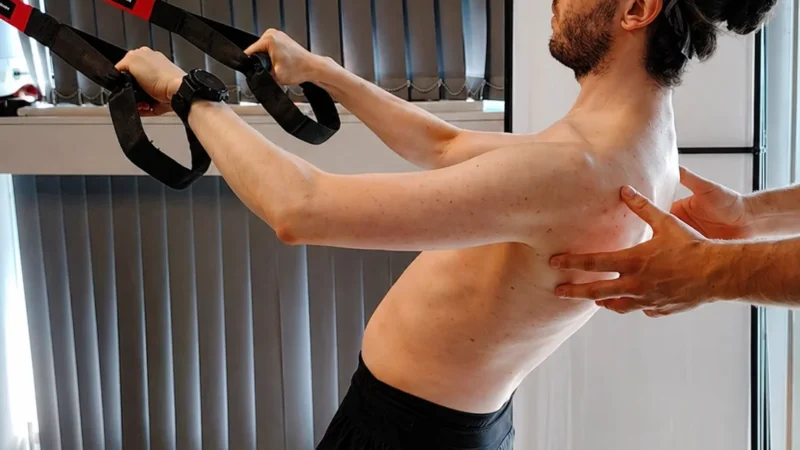 Daniel supervisa a un paciente haciendo remo bilateral con un TRX en Infinitum Corpore Bilbao